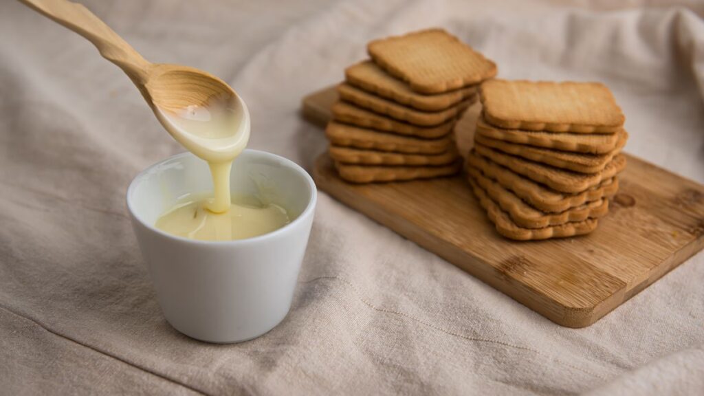 Sweetened Condensed Milk in white bowl in front of cookies.