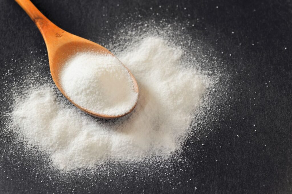 Baking soda in wooden spoon on black background.