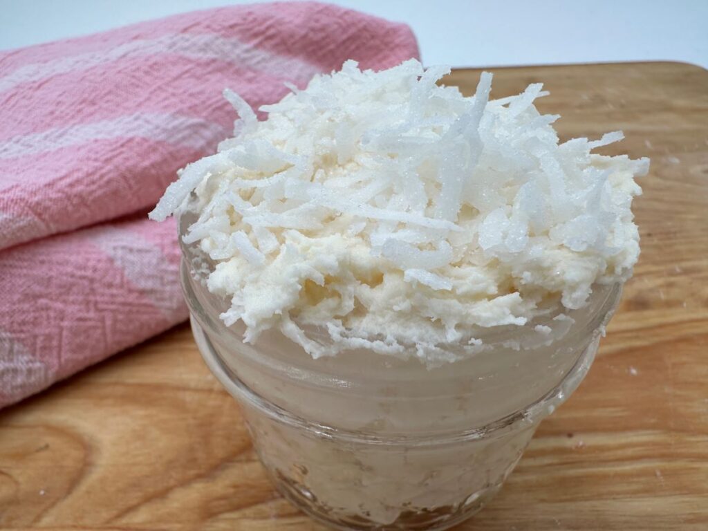 White frosting in clear glass jar with shredded coconut on top.