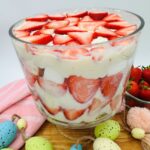 Layered strawberries, cream, and white cake in clear glass bowl.