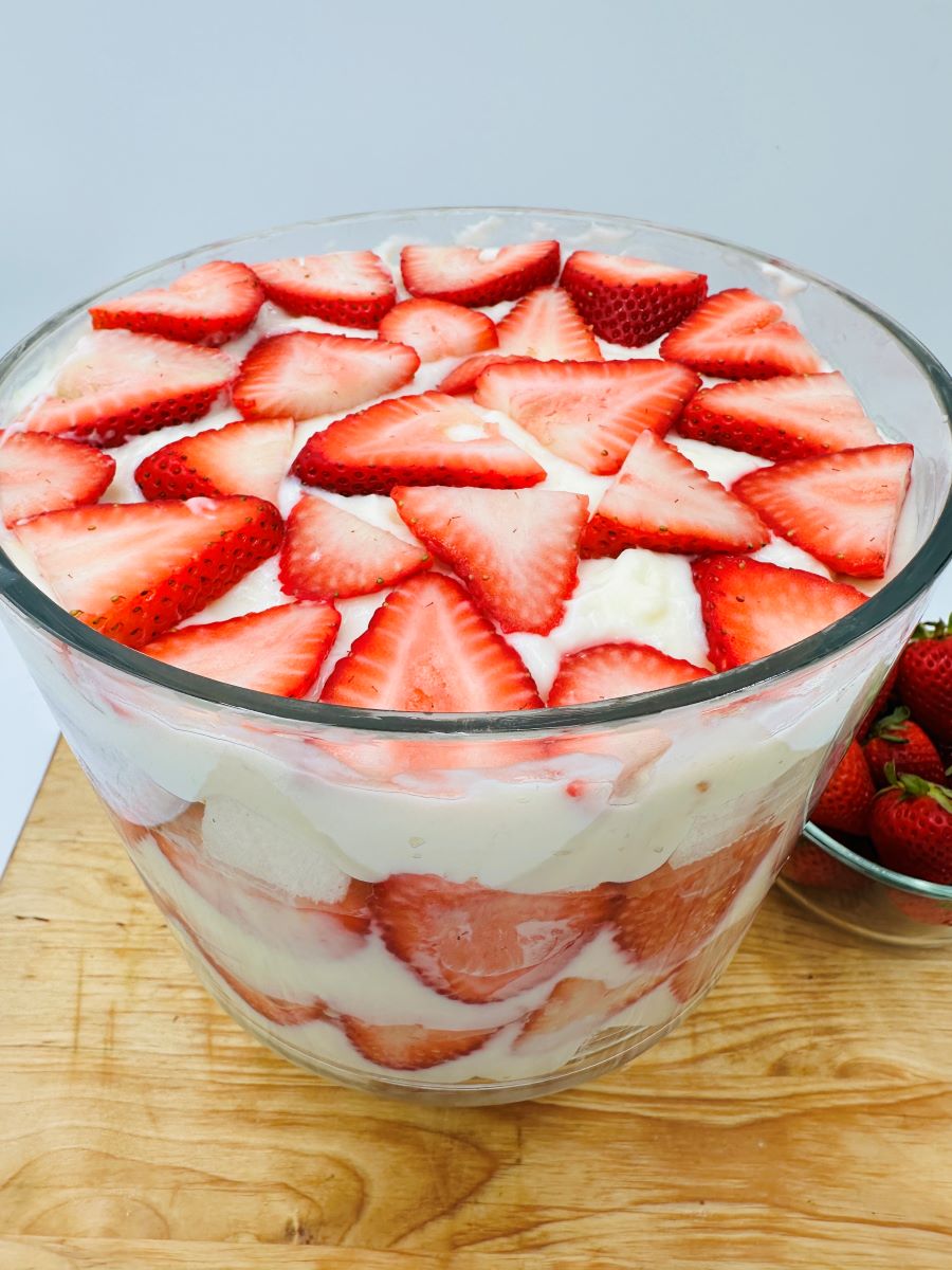 Layered strawberries, cream, and white cake in clear glass bowl.
