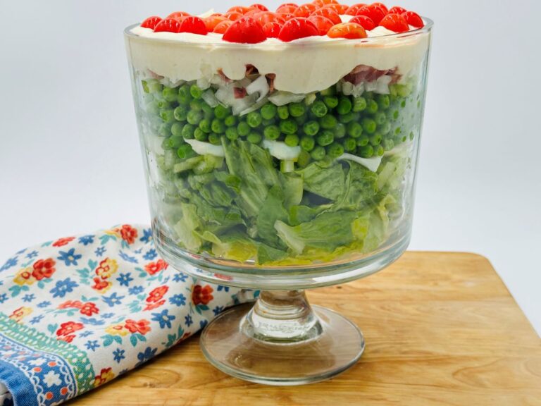 Layered green salad in clear bowl with mayonnaise and cherry tomatoes on top.