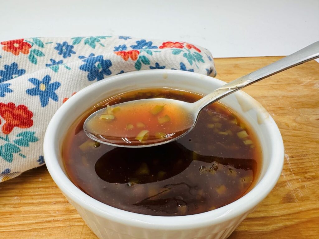 Spoon filled with brown sauce over white bowl of same sauce.