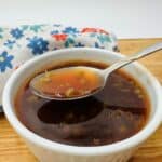 Spoon filled with brown sauce over white bowl of same sauce.