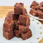 Stack of fudge on white plate with plate of fudge in background.