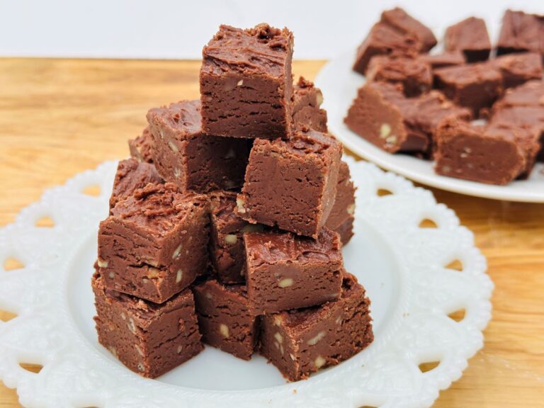Stack of fudge on white plate with plate of fudge in background.