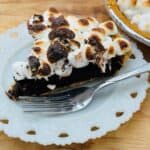 S'mores pie slice with fork in front on white plate.