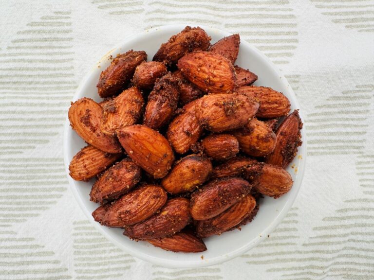 Spiced almonds in white dish on white and grey tablecloth.