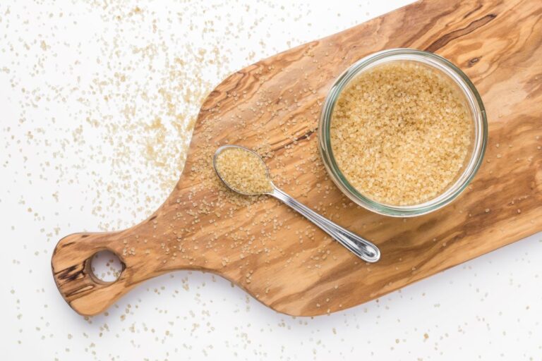 Top view of brown sugar in glass jar next to spoon on wooden board.