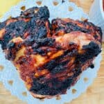Three barbecue chicken thighs on white plate with white bowl of barbecue sauce in background.