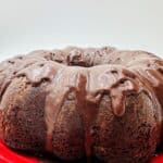 Chocolate bundt cake with fudge glaze on red plate.