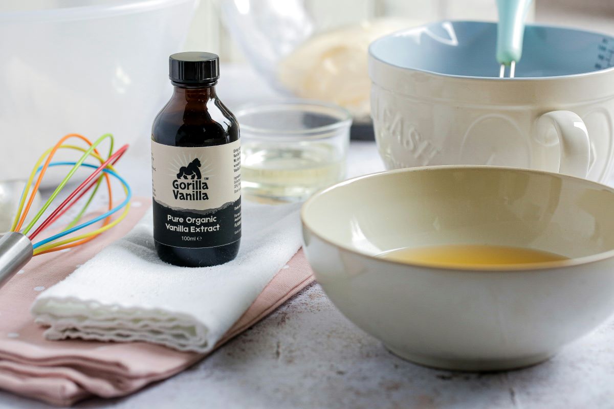 Bottle of vanilla extract on white towel surrounded by mixing bowls and whisk.