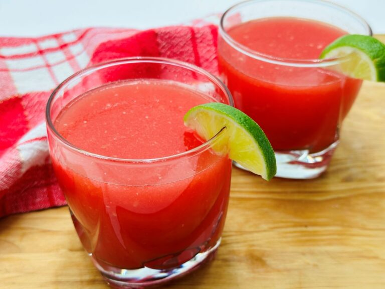 Two clear glasses of red watermelon juice on wooden board.