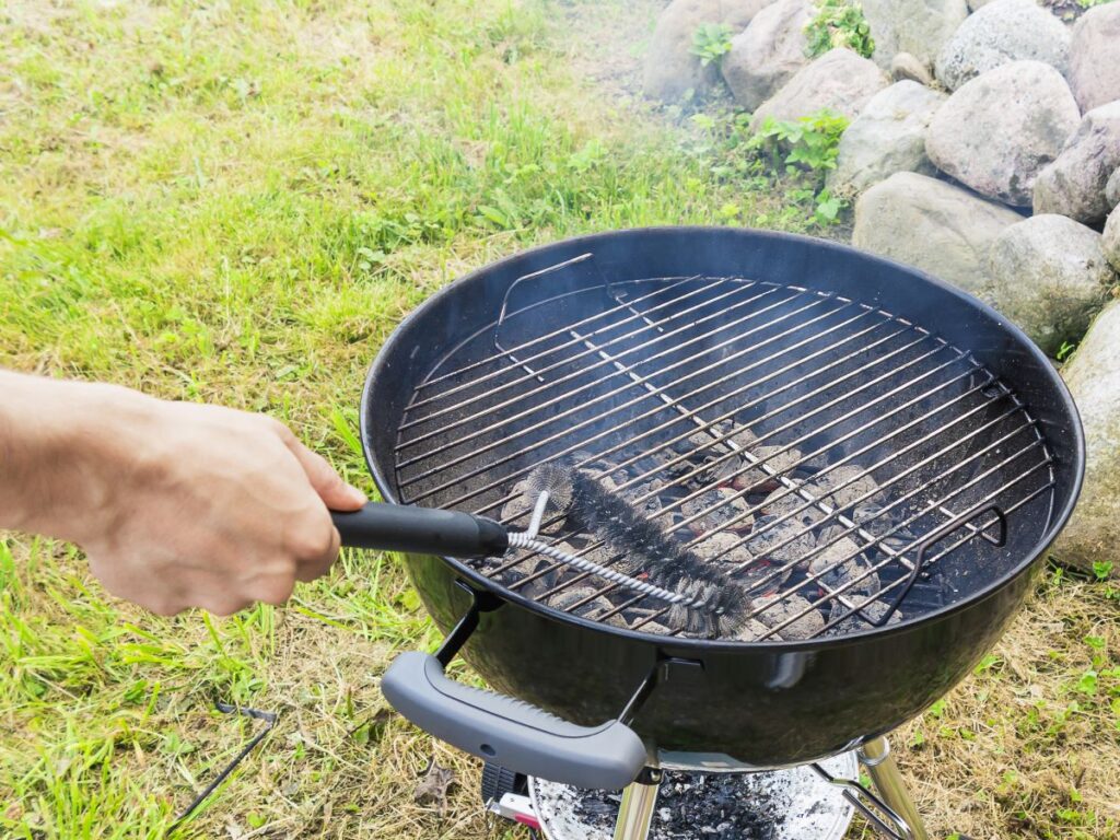Hand using wire brush to clean charcoal grill.