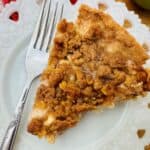 Top view of apple pie slice on white plate next to fork.