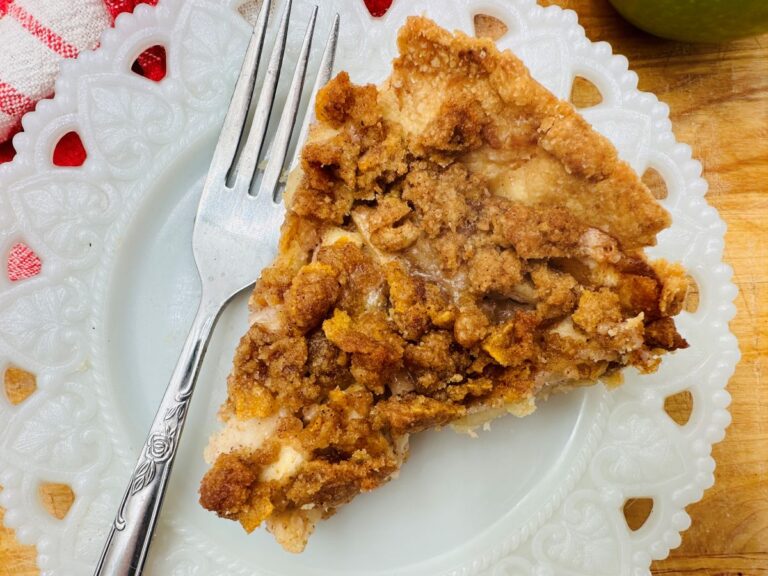 Top view of apple pie slice on white plate next to fork.