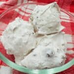 Three pieces of divinity candy in a clear glass bowl, placed on a red and white checkered cloth.