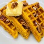 Three triangular orange waffles topped with syrup, butter, and pecans on white plate.