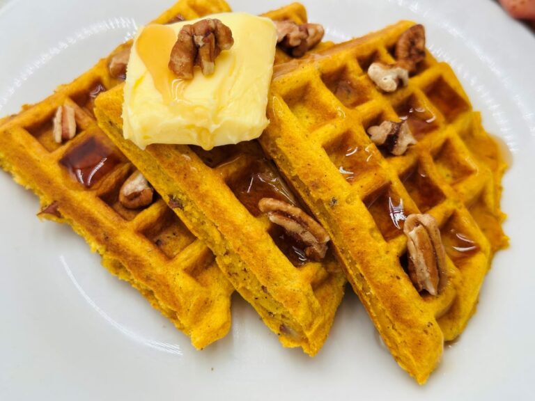 Three triangular orange waffles topped with syrup, butter, and pecans on white plate.