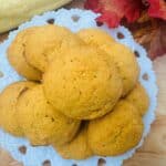 Pile of orange cookies on white plate with wooden background.