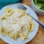 Tortellini with white sauce and pepper on white plate with fork.