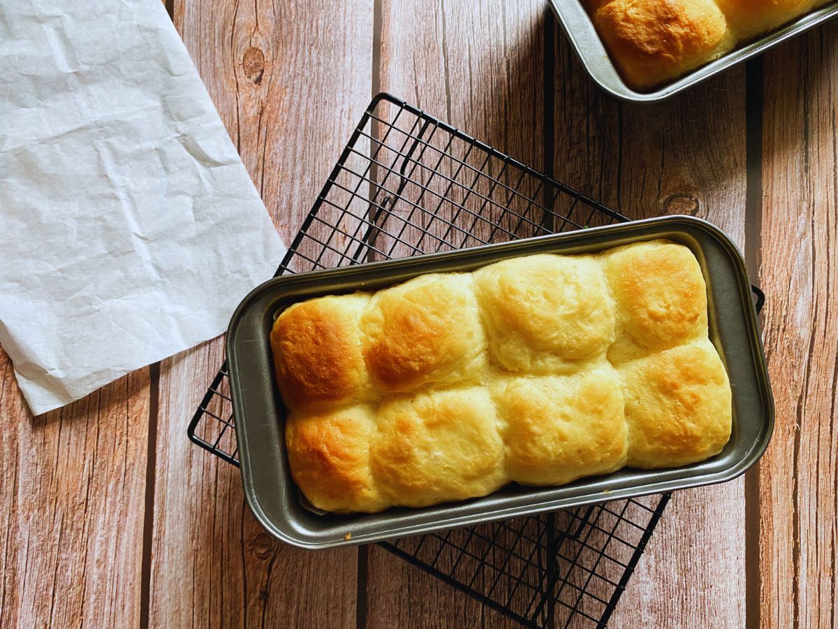 Metal rectangular bread pan with cooked bread inside on wooden background.