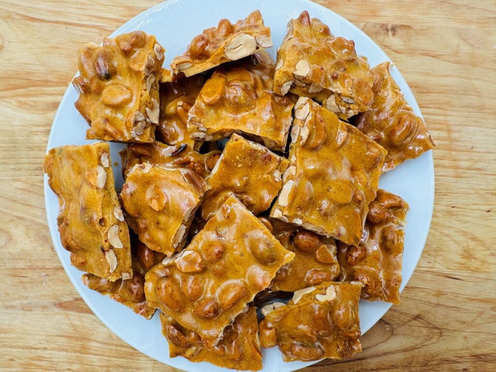 Pile of peanut brittle on white plate.