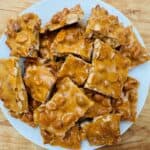 Pile of peanut brittle on white plate.