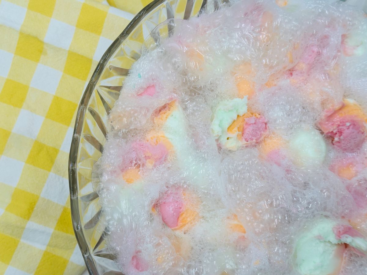 Overhead view of half of clear glass bowl filled with rainbow ice cream and clear bubbles.