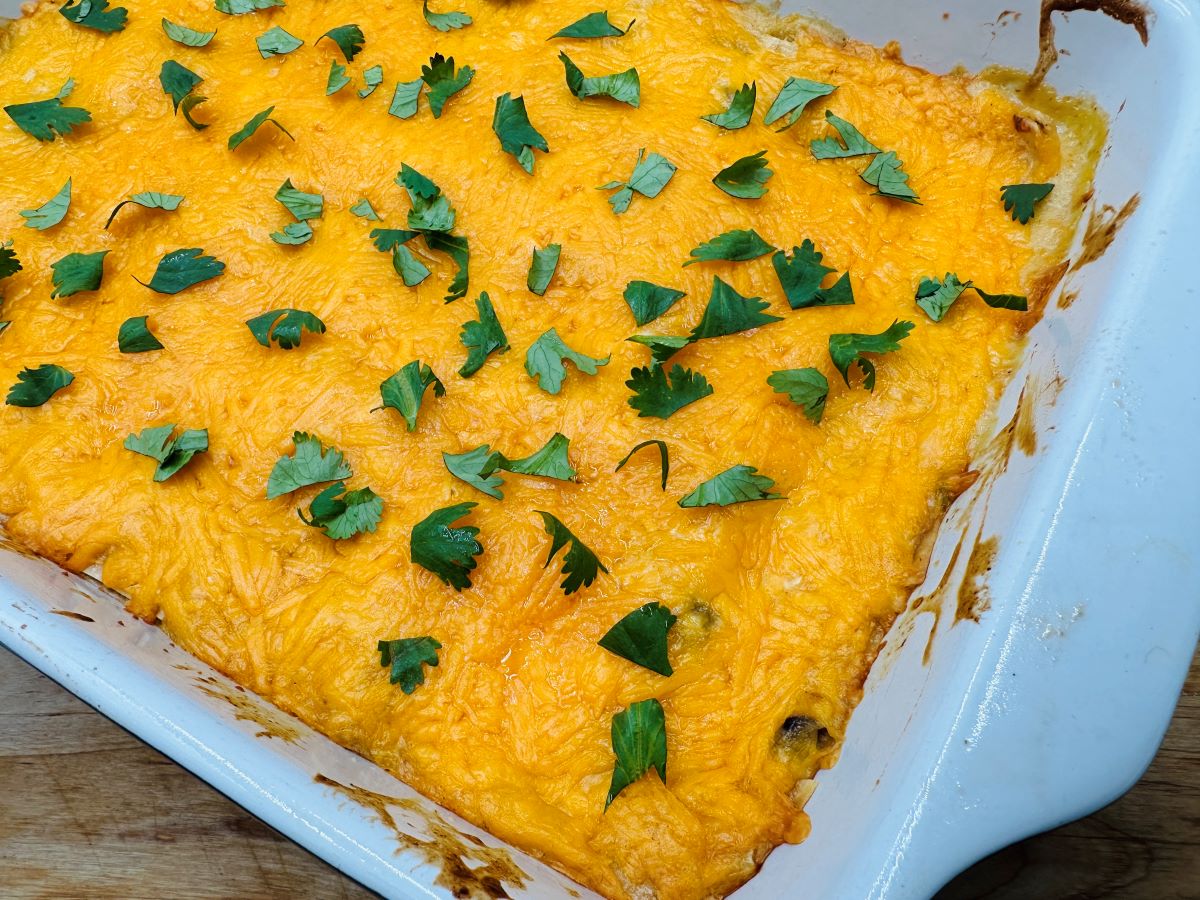 Overhead view of melted cheese cheddar cheese with green cilantro in white casserole dish.
