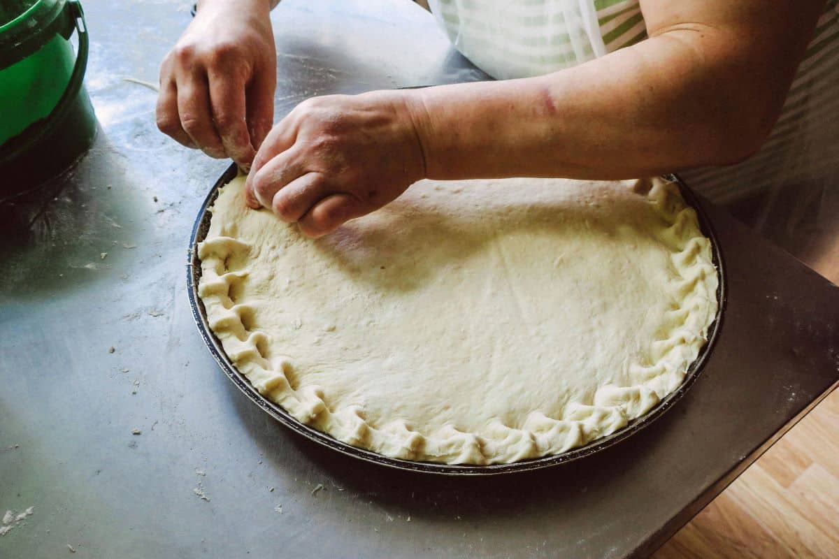 Hands making top pie crust.