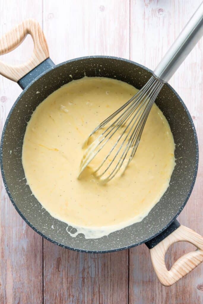 Light yellow sauce in gray pot with whisk.