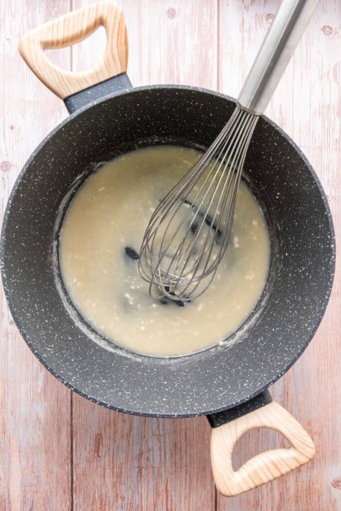 Light yellow sauce in gray pot with whisk.