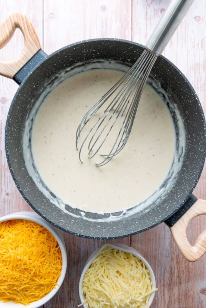 Creamy white sauce in gray pot with whisk.