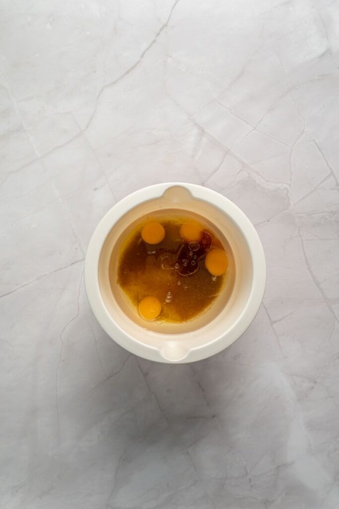 Top view of light brown liquid with yellow egg yolks in white bowl.
