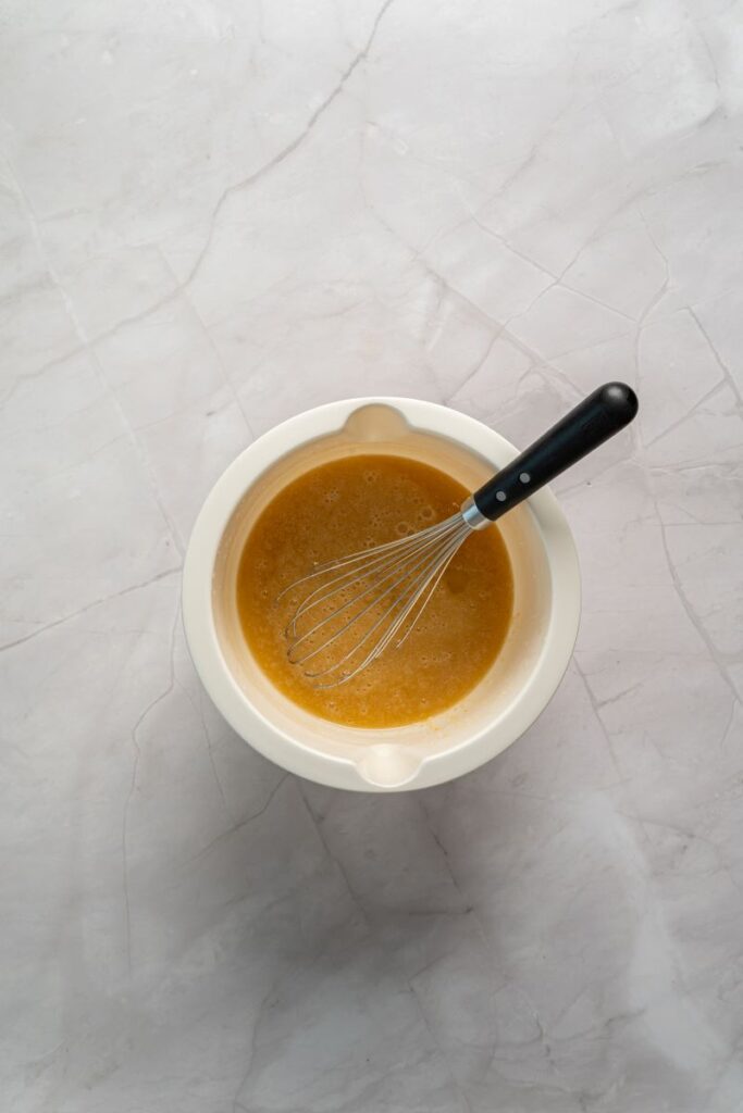 Top view of light brown liquid with whisk in white bowl.