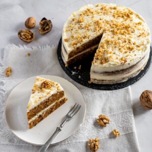 Top view of slice of carrot cake on white plate with fork below whole carrot cake with one slice missing.