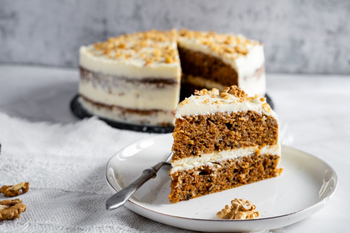 Front view of slice of carrot cake on white plate with fork in front of carrot cake with slice missing.