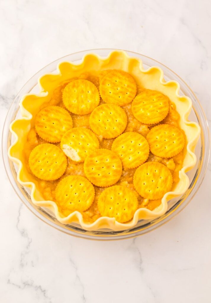 Uncooked pie curst topped with filling and whole Ritz crackers.