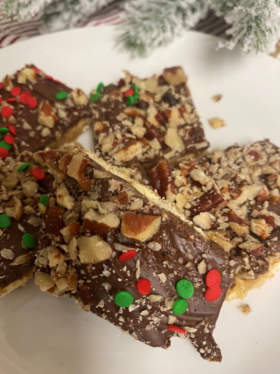 Saltine toffee in pile in white plate with Christmas tree branches in background.