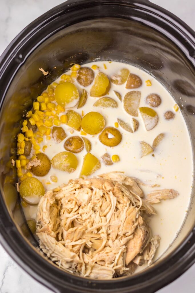 Shredded chicken, potatoes, corn, and cream in slow cooker.