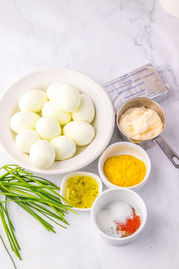 Ingredients for deviled egg dip in white bowls on marble counter.