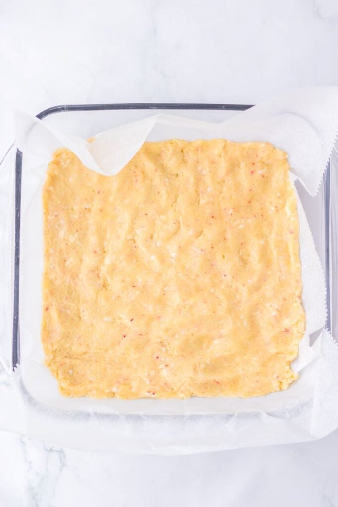 Tan cookie dough pressed into clear square glass dish.
