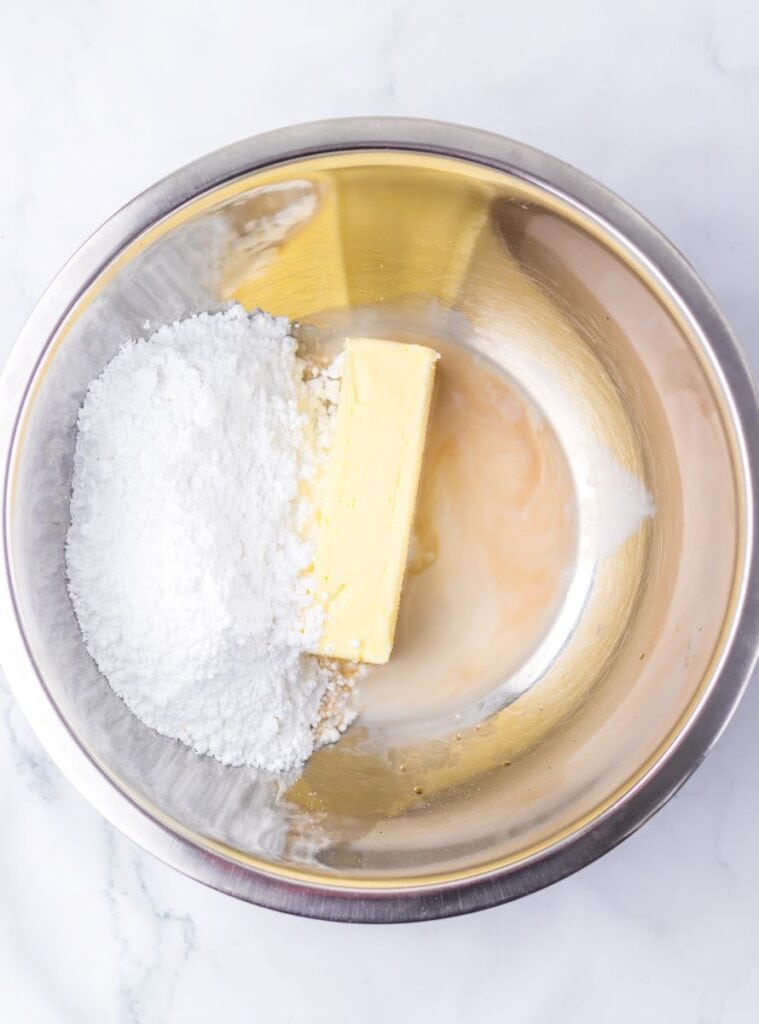 Powdered sugar, butter, milk, and vanilla in silver bowl.