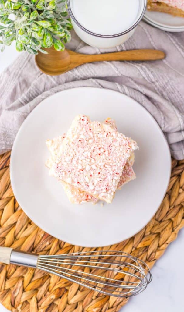 Top view of three light brown cookie bars with red and white speckled frosting stacked on white plate.
