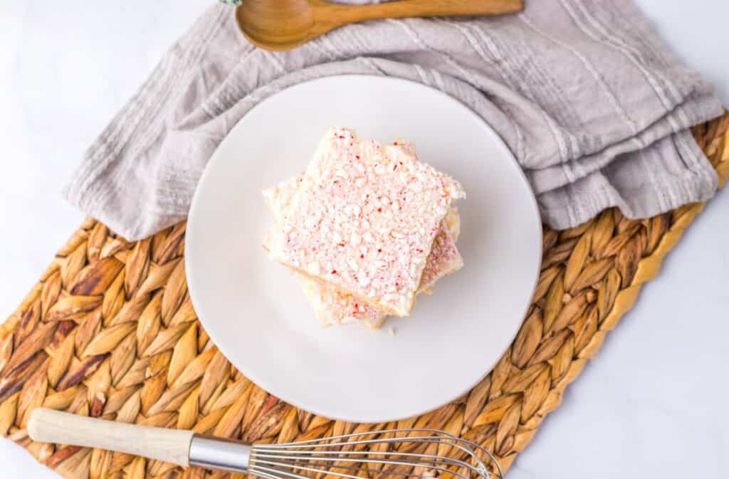 Top view of three light brown cookie bars with red and white speckled frosting stacked on white plate.