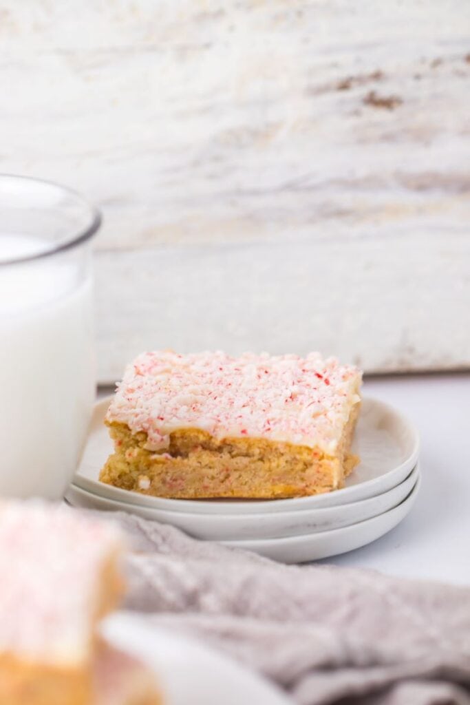 Light brown cookie bar with red and white speckled frosting on white plate.