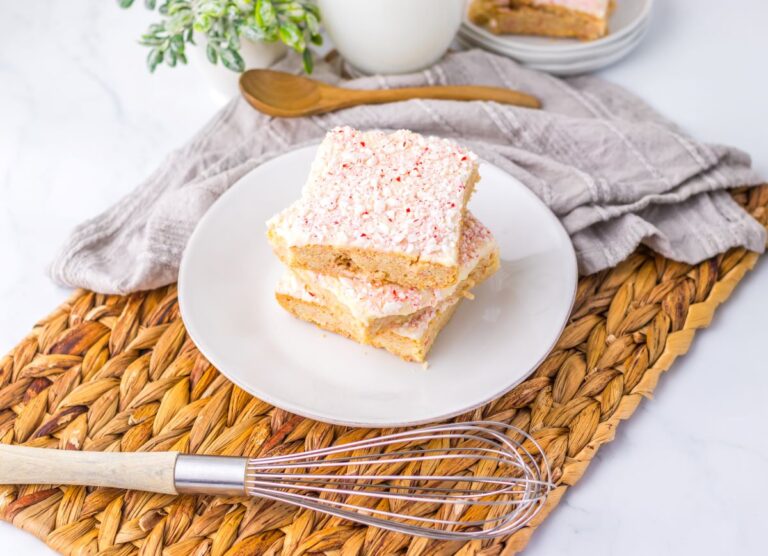 Three light brown cookie bars with red and white speckled frosting stacked on white plate.