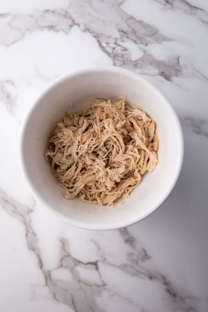 Top view of shredded chicken in white bowl.
