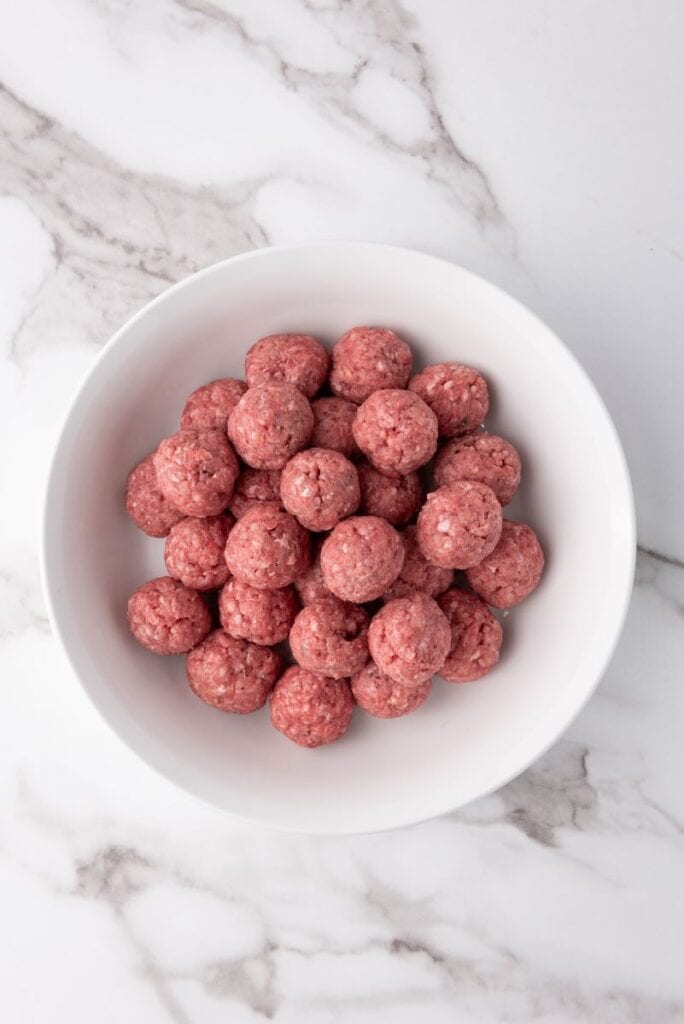 Raw ground beef meatballs in white bowl.